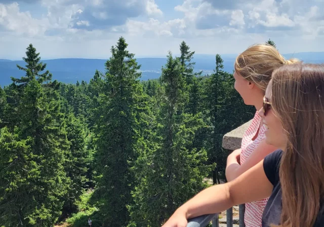 Zwei Frauen blicken von einem Balkon auf einen Wald