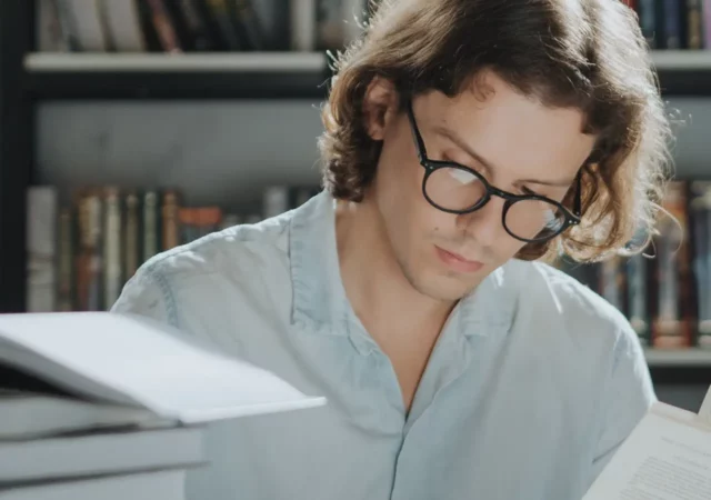 Ein Mann mit Brille liest in einer Bibliothek ein Buch