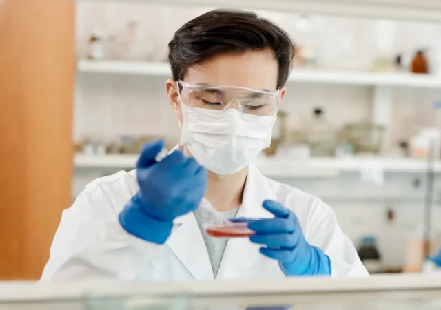 Ein Mann mit Maske und Handschuhen arbeitet an einer Petrischale im Labor.